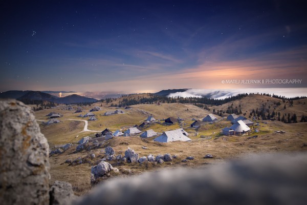 The Velika planina wooden cottage settlement lit by the moonlight on late november evening. In the distance to the right the river of clouds flows towards the Menina plateau indicating weather change. The winter is comming ... 